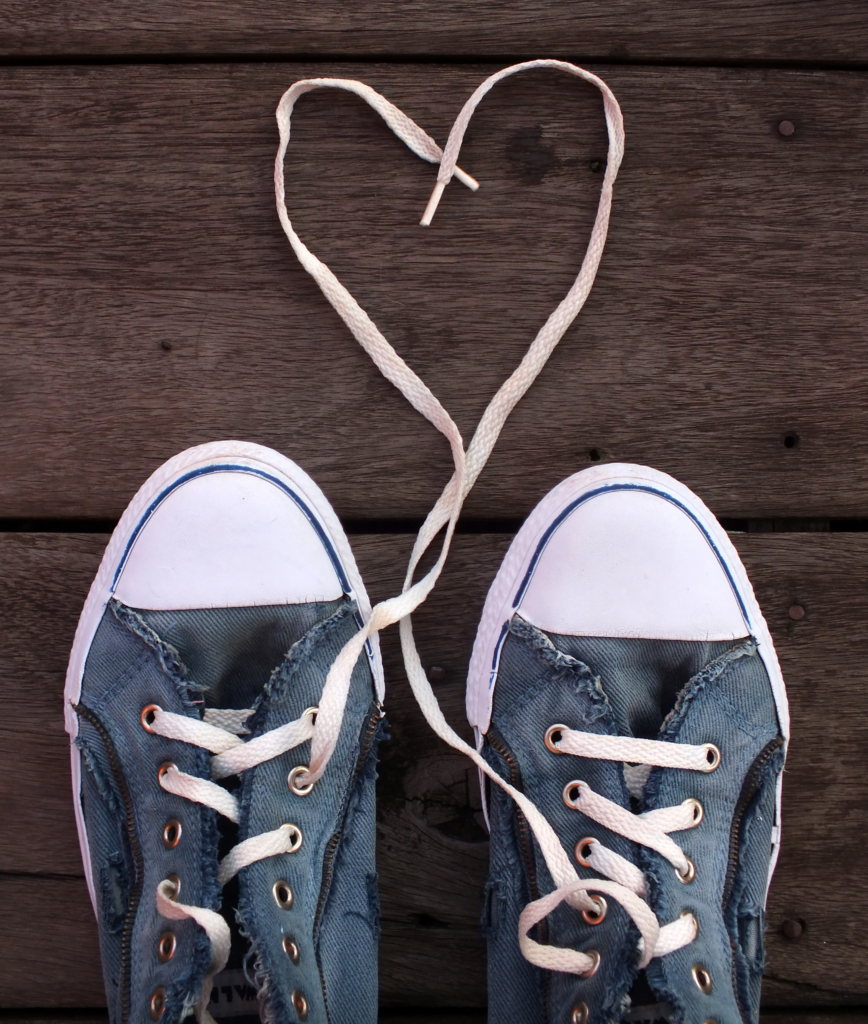 Baskets bleu jean vues d'en haut sur un plancher avec les lacets dessinant un coeur.
