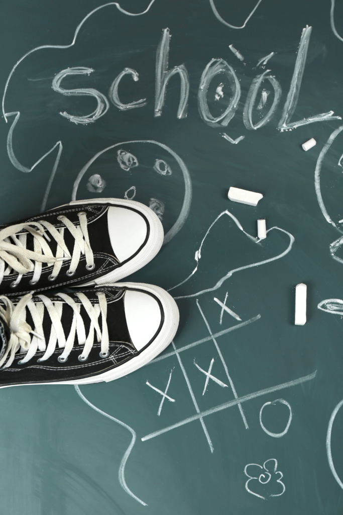 Baskets noires de type converse, vues d'en haut sur un tableau avec des dessins à la craie pour symboliser les problèmes scolaires rencontrés par les adolescents.
