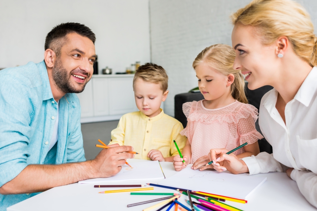 Un père, une mère, leur fille et leur fils dessinant sur une petite table.