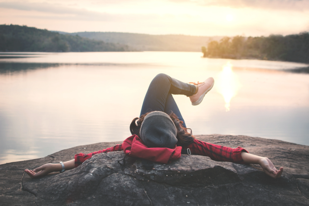 young-woman-lying-rock-by-lake-against-clear-sky